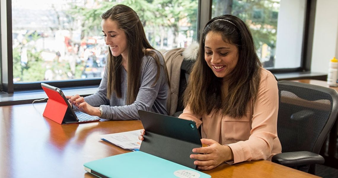 Two students sitting at a table looking at tablets